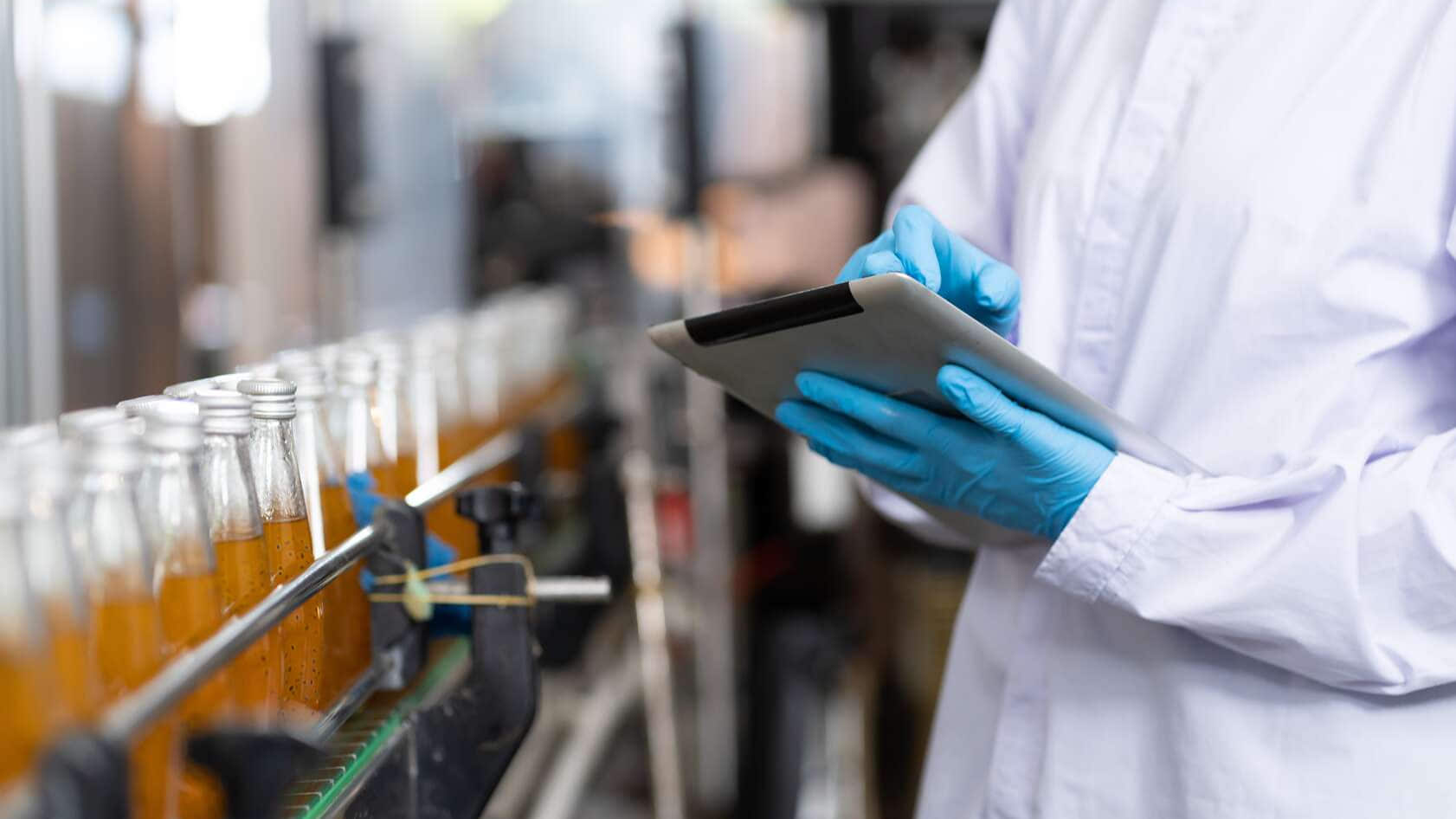 Fabricante revisando botellas de producto en un control de calidad alimentaria